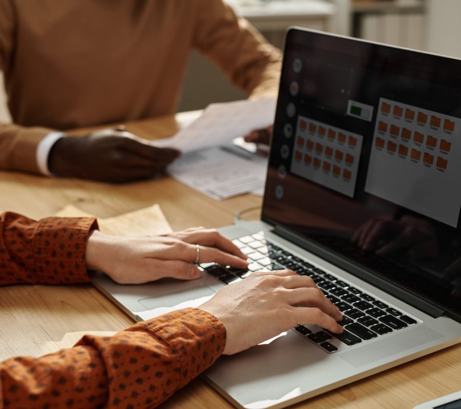 Businesswoman working on laptop at meeting Close-up of businesswoman typing on laptop while sitting at table with colleagues at meeting