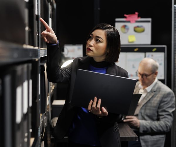 Detective in criminal archive office Asian private detective in criminal cases archive office looking for criminology file paperwork on cabinet shelves. Investigator woman surrounded by criminal case folders in agency repository room