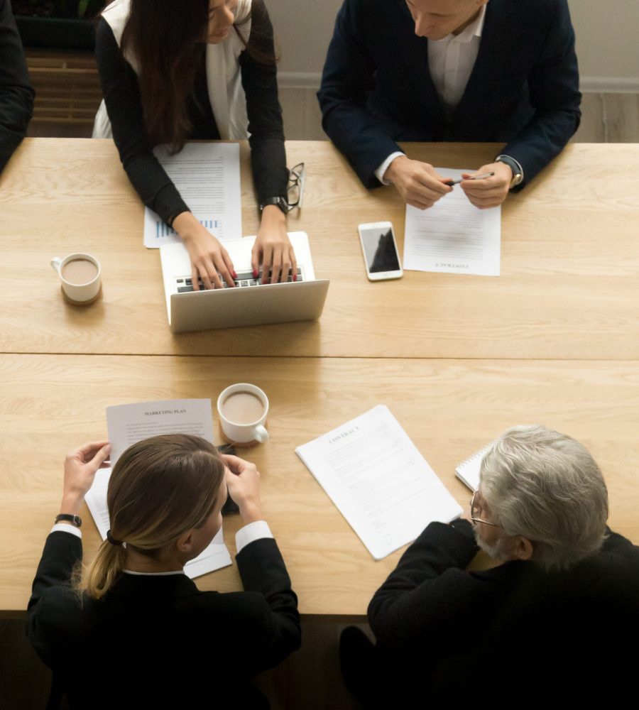 Diverse business colleagues working together at meeting, vertica Diverse business colleagues working together talking planning at meeting table, multiracial young and senior people preparing for contract negotiations talking during teamwork, vertical top view